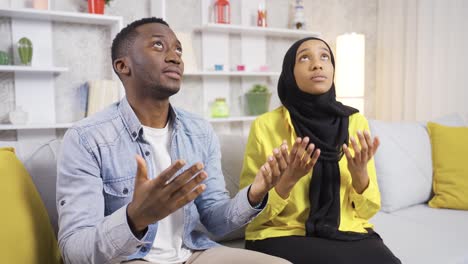 Muslim-African-married-couple-praying-at-home,-opening-their-hands-to-Allah.